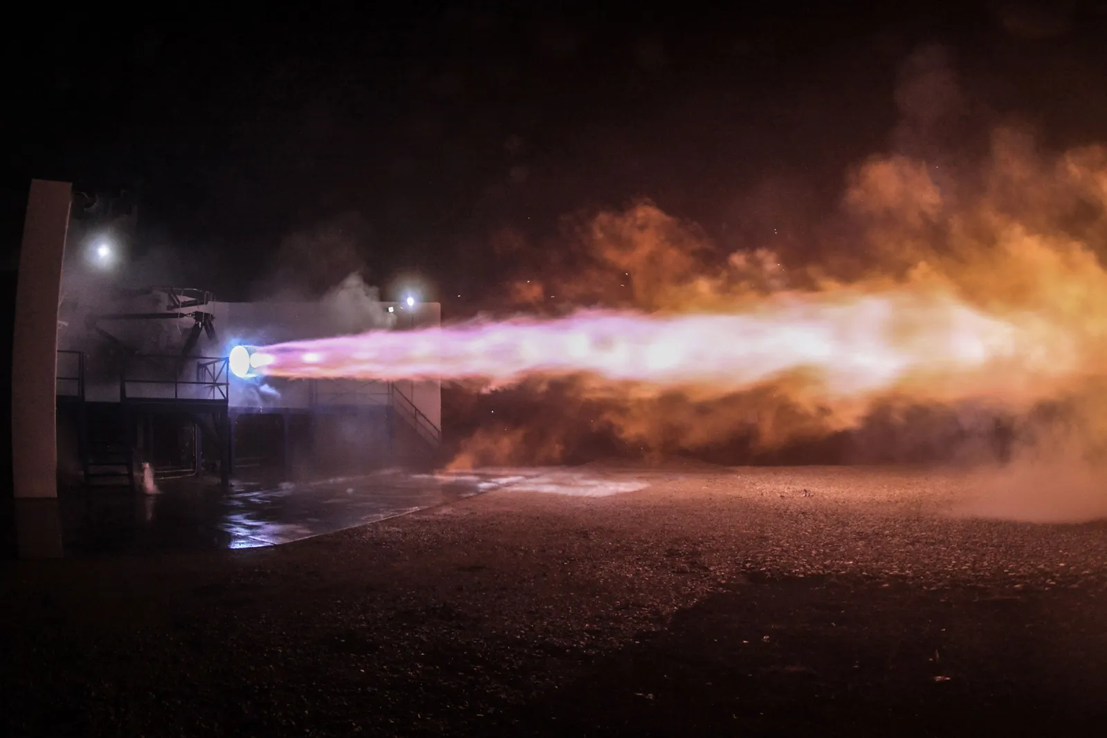 Nighttime rocket engine hot-fire test on an outdoor propulsion test stand, a high-hazard water mist application