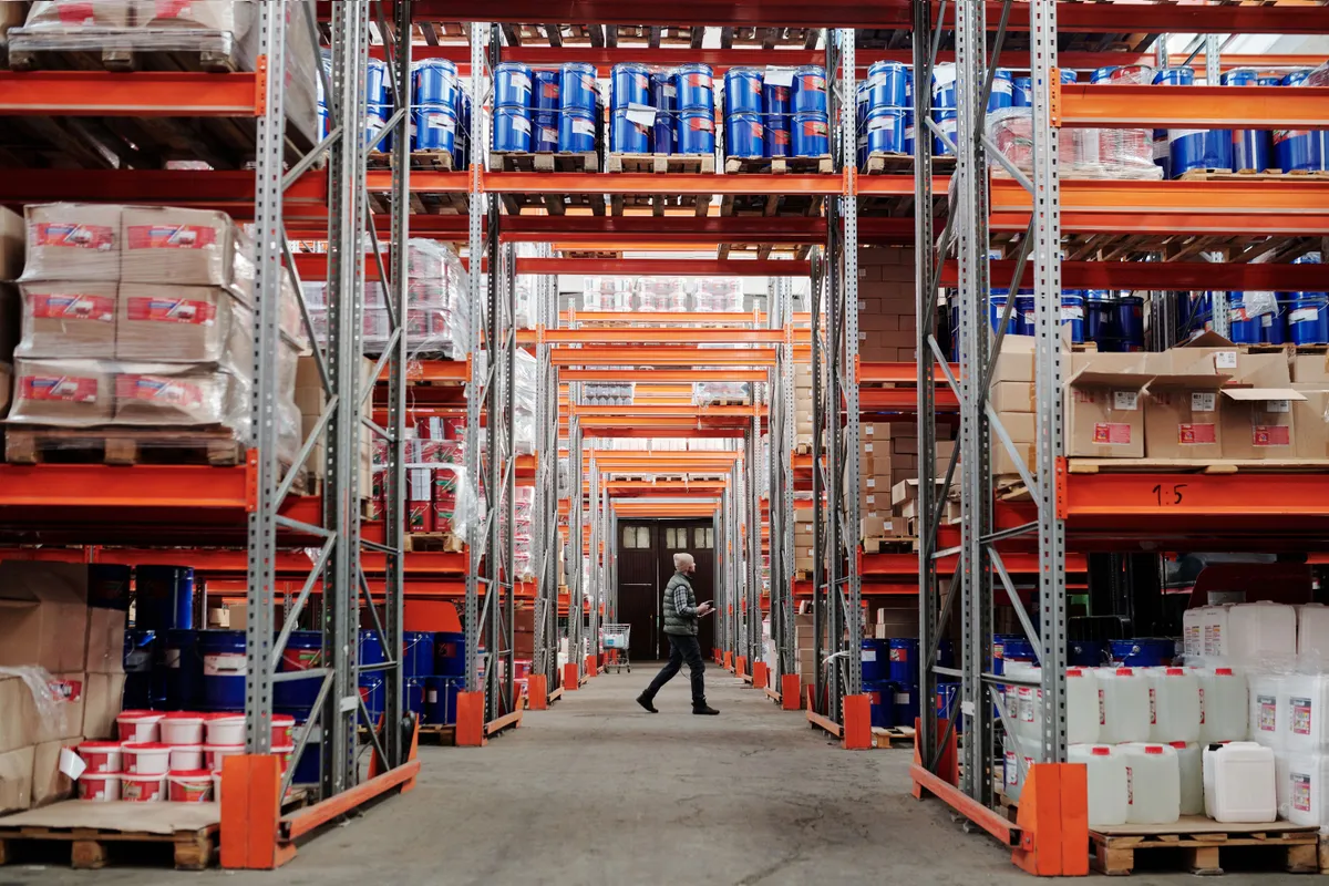 Warehouse pallet racking holding mixed commodities including paint pails, drums, and cartons