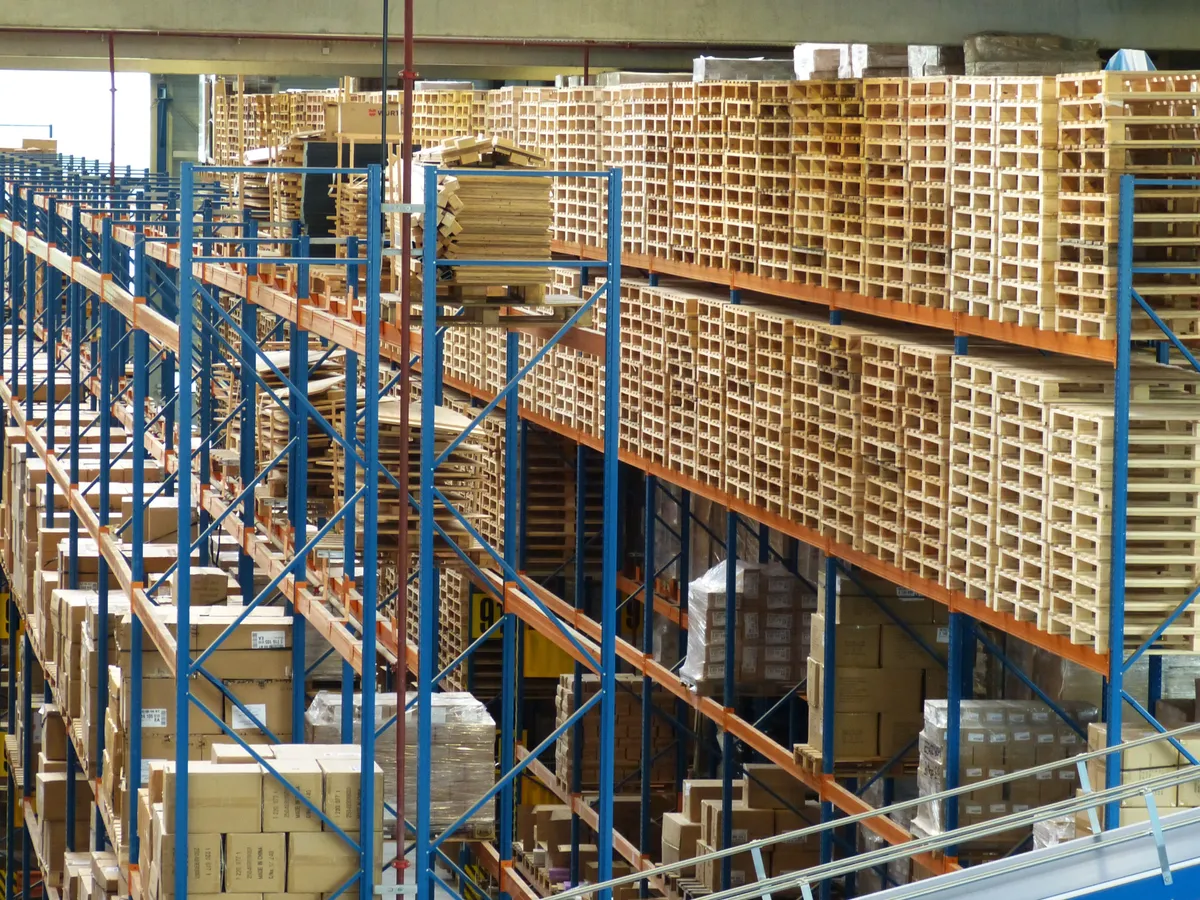 Tall warehouse pallet racks stacked with wooden pallets and an in-rack sprinkler riser